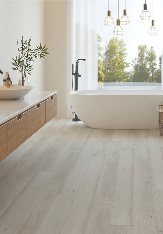 Modern bathroom with a freestanding white bathtub near a large window, luxury vinyl plank flooring, floating wood vanity with a sink, potted plant, and pendant lights hanging from the ceiling.