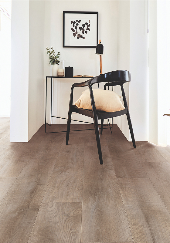 A minimal home office with light wood flooring, a black chair with a beige cushion, a small black desk with decor items, and framed abstract art on a white wall.