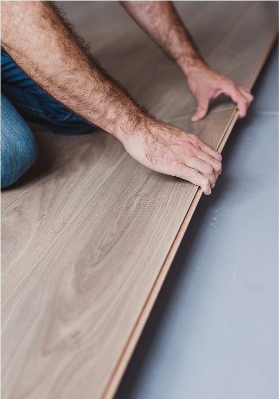 A person installs light wood laminate flooring, carefully aligning the planks with their hands.