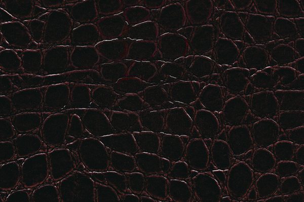 Modena Brown features a dark brown, glossy finish with a textured surface that mimics crocodile or alligator skin, showcasing irregular, raised, interconnected patterns and subtle highlights along the edges of each scale.