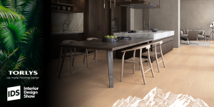 A modern kitchen and dining area with light wood flooring, dark wood cabinets, marble countertops, and minimalist chairs. TORLYS IDS 2022 logos appear on the left side of the image.