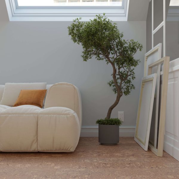 A cozy, modern living space features the Burl Natural plush white sofa with an orange cushion, a potted tree, and empty picture frames leaning against a wall beneath a skylight.
