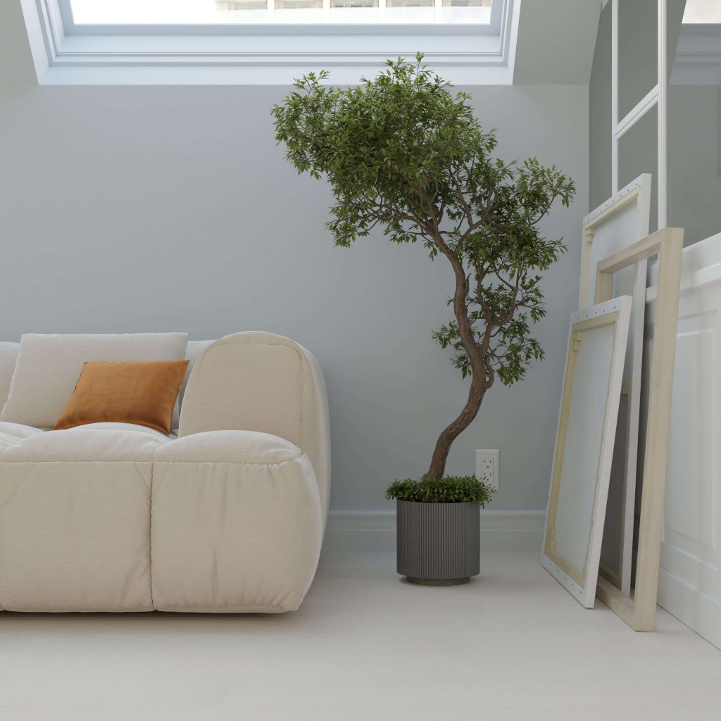 A contemporary living space featuring the Paseo Fulwell cream sofa, accented with an orange cushion, a potted tree, and empty picture frames leaning against the wall beneath a skylight.