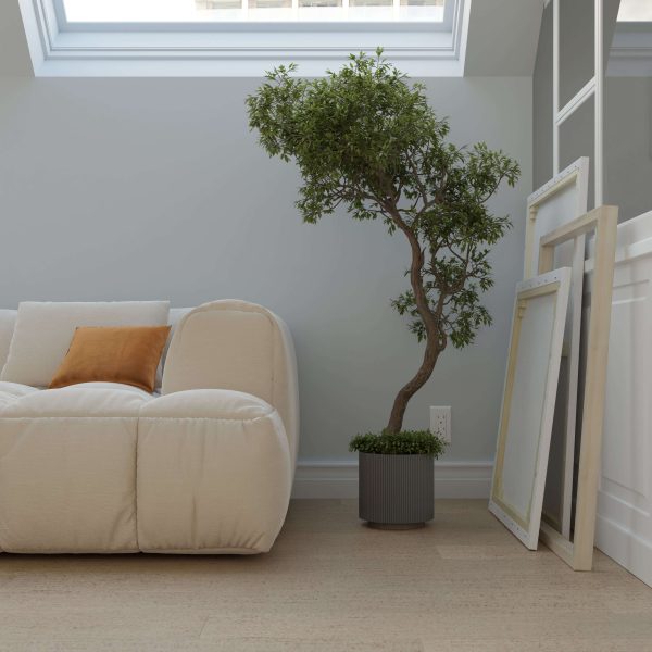 A minimal living room featuring the Paseo Aspen plush white sofa, an orange cushion, a potted tree, and empty picture frames resting under a skylight window.