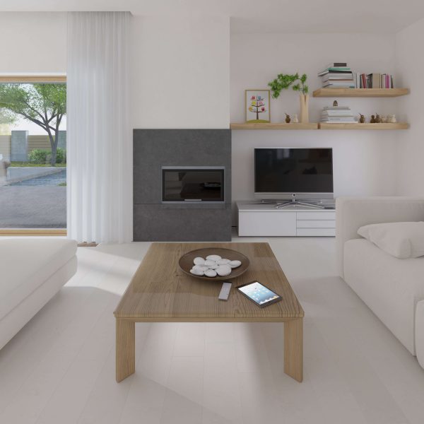 A modern, minimalist living room featuring the Burl Linden wooden coffee table with a bowl and tablet, white furniture and walls, shelves with books and plants, a TV, and large windows overlooking greenery.