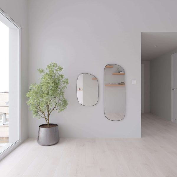 A minimalist room with light walls and Cumulus Oak flooring, a potted plant on the left, two uniquely shaped wall mirrors, floating shelves reflected in them, and natural light streaming from a large window.