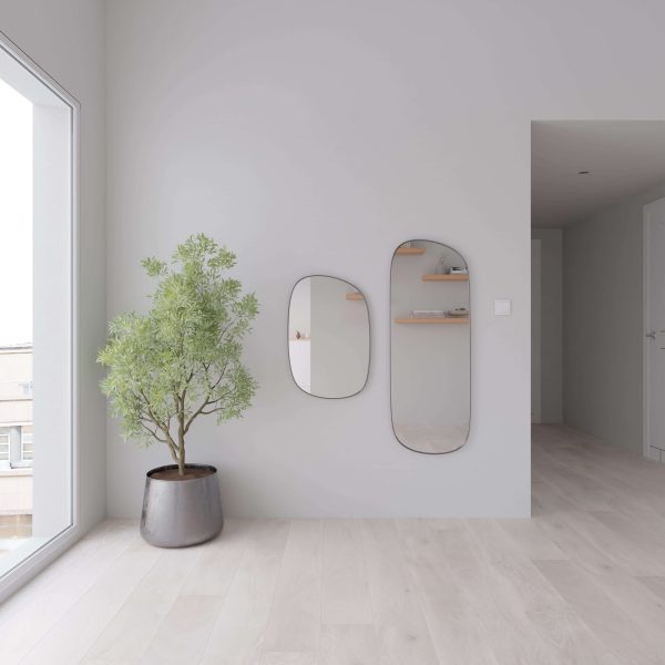 A minimalist room features Fairwinds Oak* light wood floors, a potted plant by a large window, and two modern, irregular mirrors on a white wall reflecting shelves with decor.