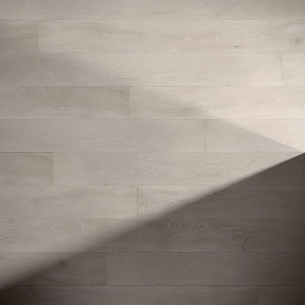 Fairwinds Oak* flooring features horizontal light wood planks with visible grain, partially covered by a large diagonal shadow that contrasts the bright sunlit area with the shaded section.