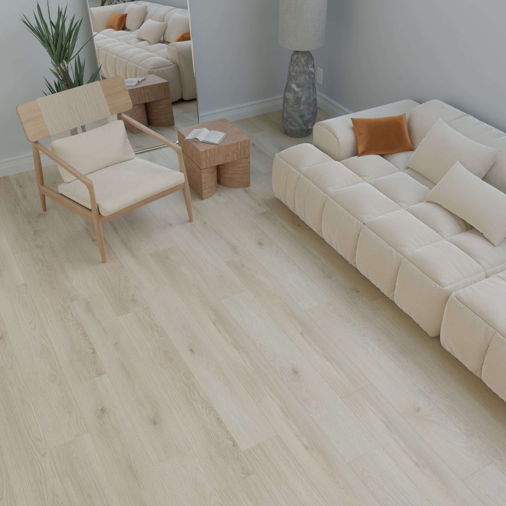 A minimal living room featuring the O'Hara beige tufted sofa with pillows, light wood flooring, a wooden chair with woven seat, two small wooden tables, a tall lamp, a potted plant, and a large mirror against the wall.