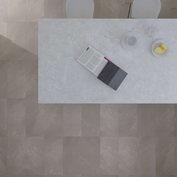 A top-down view of the Cliff Island table styled with an open book, white teapot, cup, and a small bowl of lemon slices. Two white chairs sit nearby on a gray tiled floor.