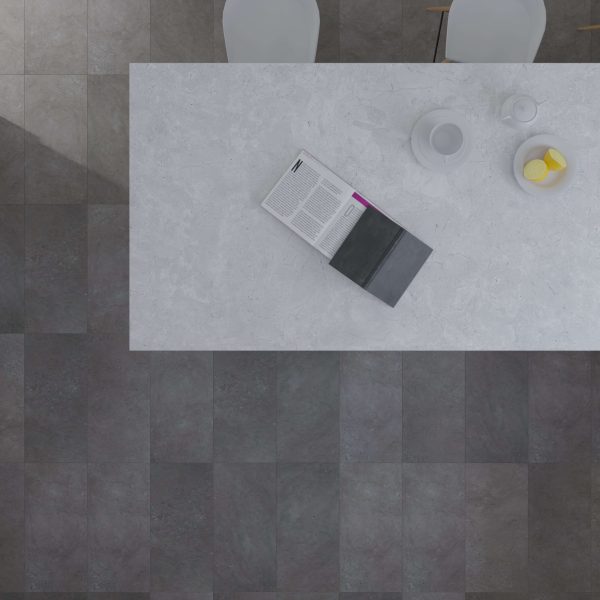 A top-down view of a white marble Cambridge table with an open magazine, black notebook, teapot, cup, and bowl of lemons. Two white chairs sit at the table on dark, square-tiled flooring.