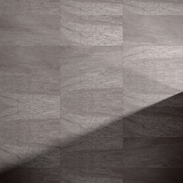 Close-up of a Cenere Grey tiled floor with a stone-like texture. A diagonal shadow crosses the lower right corner, highlighting the contrast between illuminated and shaded areas.