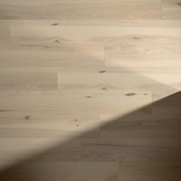 Maffra* features light-colored wooden floor panels with subtle grain patterns and small knots, while a diagonal shadow partially covers the bottom right corner, creating contrast on the smooth, natural wood surface.