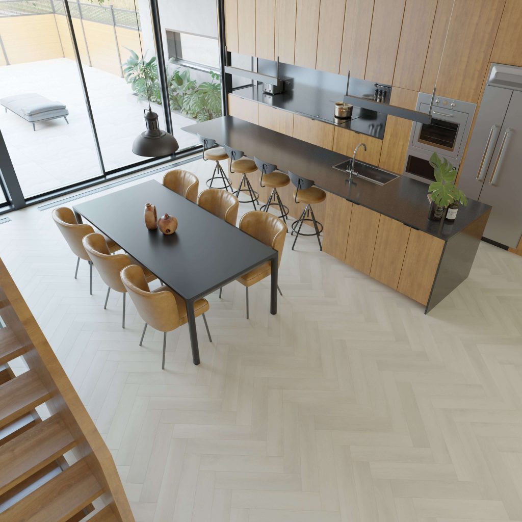 The Glenbrook* kitchen and dining area features wood cabinets, black countertops, barstools, a black dining table with tan chairs, large windows for natural light, and decorative plants.