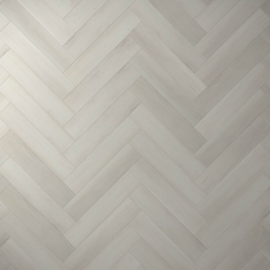 Glenbrook* features a light gray wooden floor in a herringbone pattern, with smooth, evenly finished planks laid diagonally to create a repeating V-shaped design.