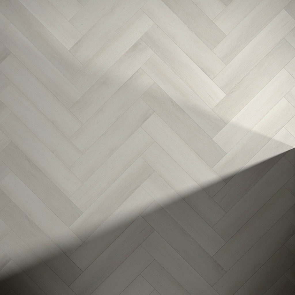 A Glenbrook* light herringbone-patterned wooden floor with a diagonal shadow cast across the lower right corner.