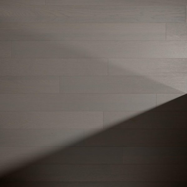 A diagonal shadow falls across a smooth, matte-finished Silver Rock Oak* floor composed of evenly spaced, rectangular planks in varying shades of gray.