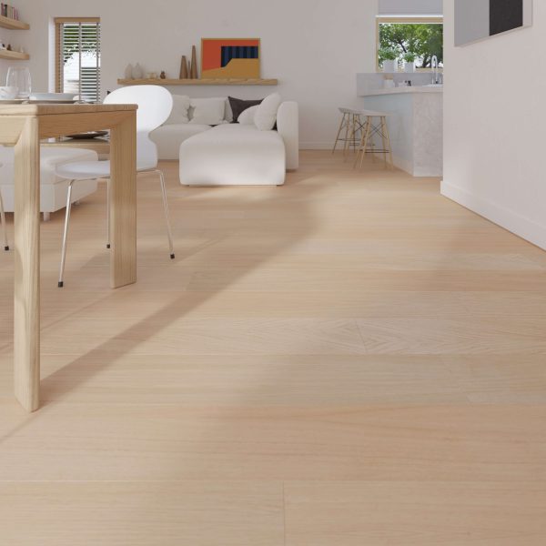 A modern living and dining area featuring Briar Oak R&Q flooring, a wooden dining table with white chairs, a white sofa, minimal shelf decor, and a kitchen with bar stools in the background.