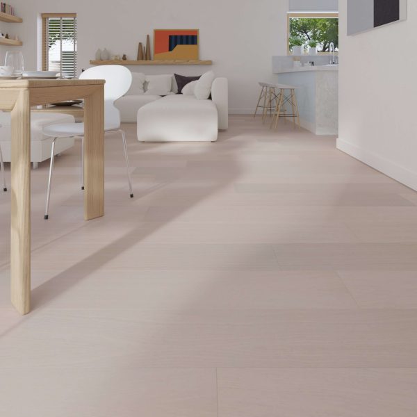 A modern, minimalist living and dining area features Everglade Oak R&Q* flooring, a wooden dining table, white chairs and sofa, a kitchen with barstools in the background, and sunlight streaming through the windows.