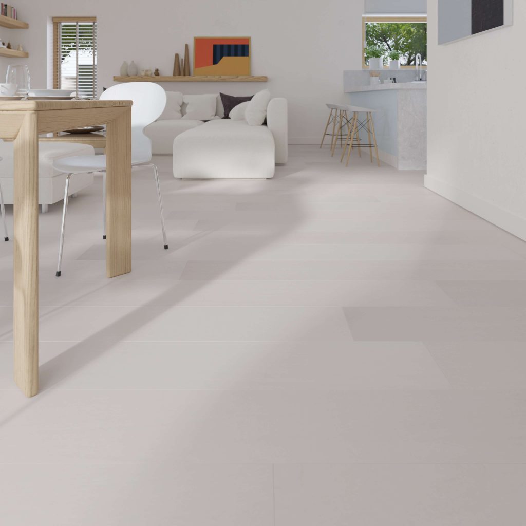 A modern living and dining area features Dove Oak R&Q* light wood flooring, a wooden dining table, white chairs, a white sofa, and minimal decor. Large windows fill the space with natural light. The kitchen is visible in the background.
