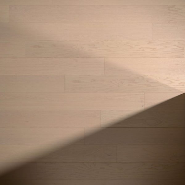 White Oak Natural Rustic* flooring features a light wood tone with visible grain and plank seams. A diagonal shadow crosses the lower right corner, highlighting the contrast between illuminated and shaded areas.