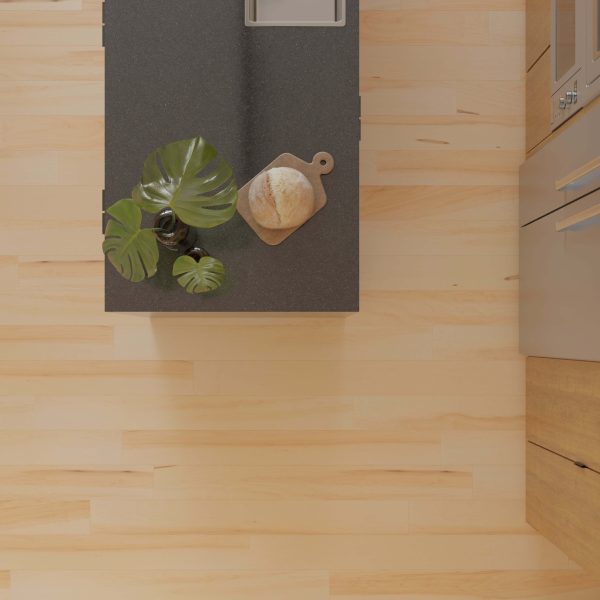 A top-down view of a modern kitchen island with a dark countertop, featuring a potted monstera, bread on a wooden board, and part of a sink; the island is surrounded by Maple Natural* light wood flooring.