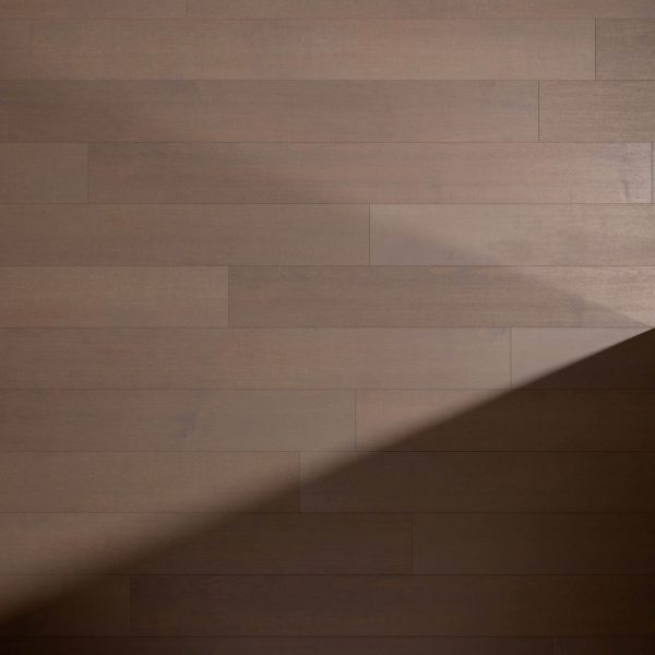 A shadow falls diagonally across a surface of light brown Maple Arabica* floorboards, creating a contrast between the lit and shaded areas. The evenly spaced boards run horizontally.