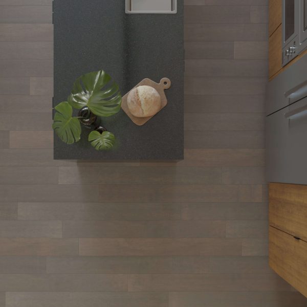A top-down view of a modern kitchen countertop featuring the Maple Latte*, with a cutting board holding a loaf of bread, a leafy green plant, sink, adjacent wooden cabinets, and a wood-patterned floor.