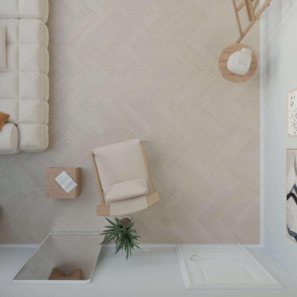 Top-down view of a minimalist living room featuring a beige armchair, round wooden side table, potted plant, sofa, and Everglade Oak* (Left) chevron-patterned floor. Decor includes a small white book and floor mirror by the white door.