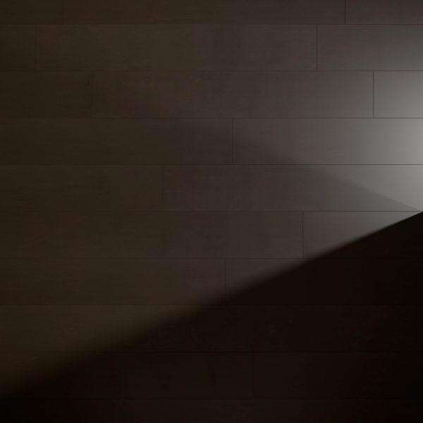 The Genova Chocolate tiles create a striking wall with deep brown tones, highlighted by a diagonal beam of light from the right, producing bold contrasts between illuminated and shaded areas on the surface.