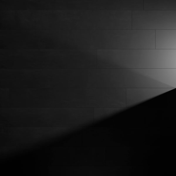 Genova Black tiles form a dark wall where a diagonal beam of light from the right creates a striking triangular contrast between lit and shadowed surfaces.