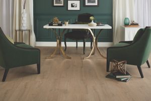 A modern home office with green walls in trending colours, a white desk with gold legs, two green armchairs, a black chair, wooden floor, and decorative items on the desk and side tables. Framed artwork hangs on the wall.