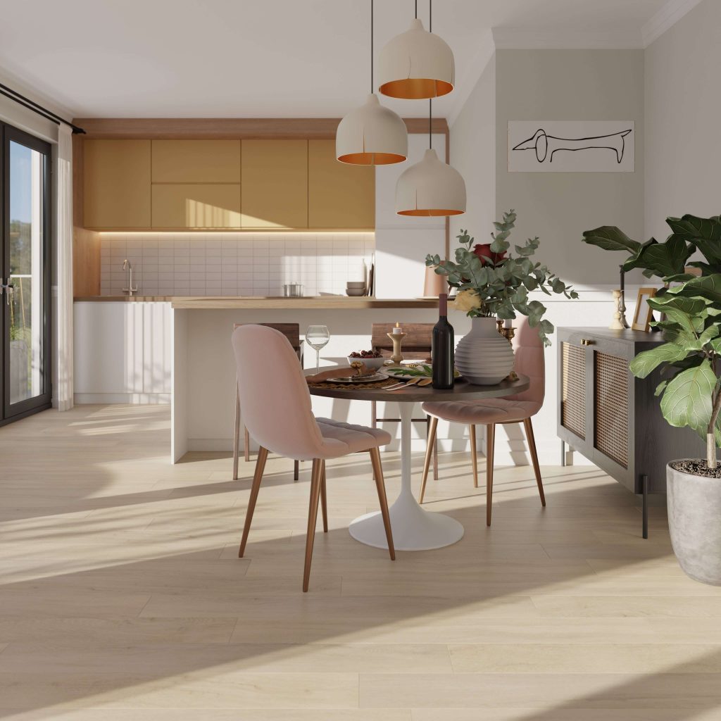 Bright modern dining area with Athens Oak round table set for two, pink chairs, pendant lights, green plants, and a minimalist kitchen in the background featuring wooden cabinets and a large window.