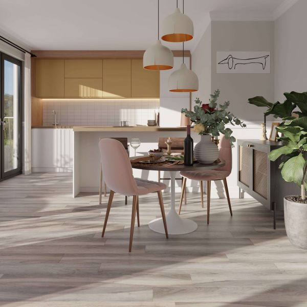 A bright modern kitchen and dining area with Rio Walnut* floors, pastel pink chairs around a round table set for a meal, potted plants, hanging pendant lights, and large windows letting in natural light.