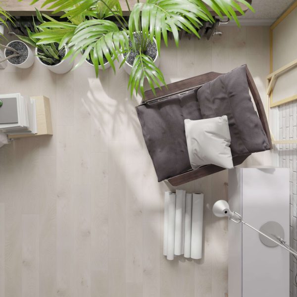 Top-down view of a cozy reading nook featuring the Lafleur* cushioned gray armchair, a white pillow, floor lamp, white cabinet, houseplants, rolled papers, and books on a light wooden floor.