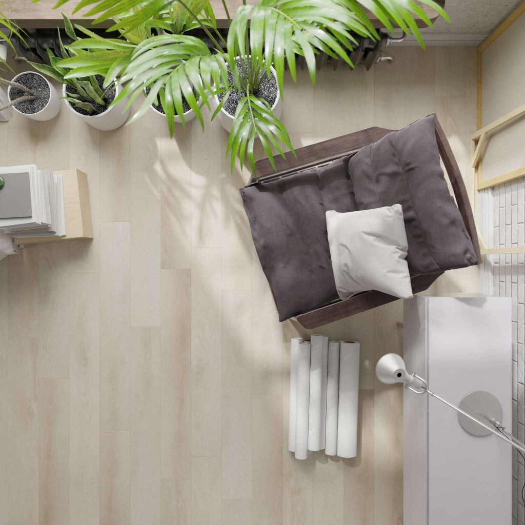 Top view of a cozy reading nook featuring the Beliveau* cushioned chair, small white pillow, potted plants, a lamp, and neatly stacked books on a light wooden floor.