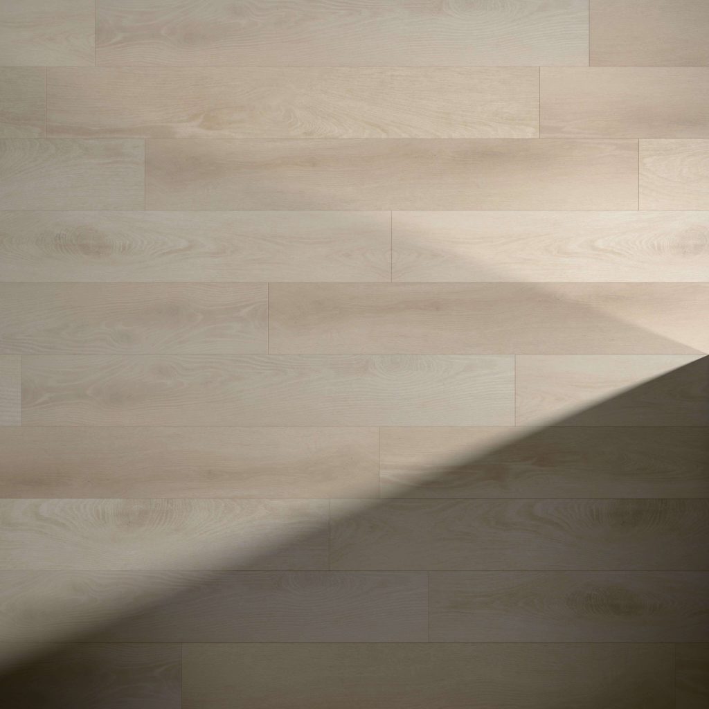 Beliveau* light wood floorboards arranged horizontally, featuring visible wood grain and a diagonal shadow crossing from the lower right to center, highlighting a contrast between illuminated and shaded areas.