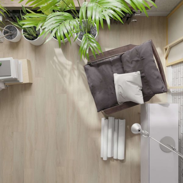 A top view of a cozy reading nook featuring the Brodeur cushioned chair, white pillow, modern lamp, rolled-up papers, green potted plants, and books arranged on light wood flooring.