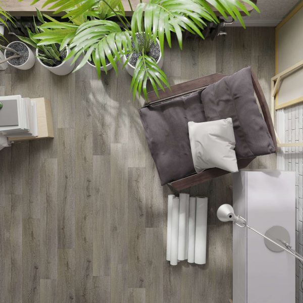 A top-down view of the Bourque* cushioned chair with a white pillow, floor lamp, books, and potted plants in a cozy reading nook on a wood-patterned floor.