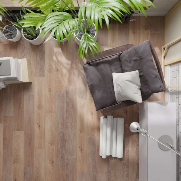 Top-down view of a cozy corner featuring the Modano* cushioned chair, white pillow, houseplants, books, rolled-up papers, a lamp, and wooden flooring—creating a comfortable and inviting workspace.