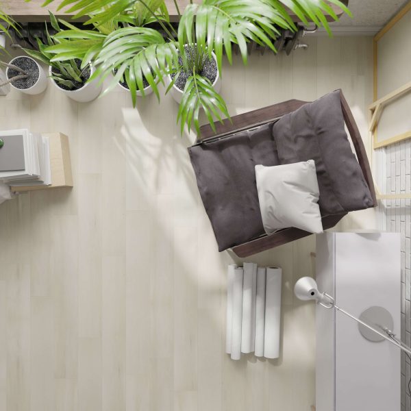 Top-down view of a cozy room corner featuring the Sittler dark cushioned chair with a white pillow, placed near a desk with rolled papers, a white lamp, indoor plants, and light wooden flooring.
