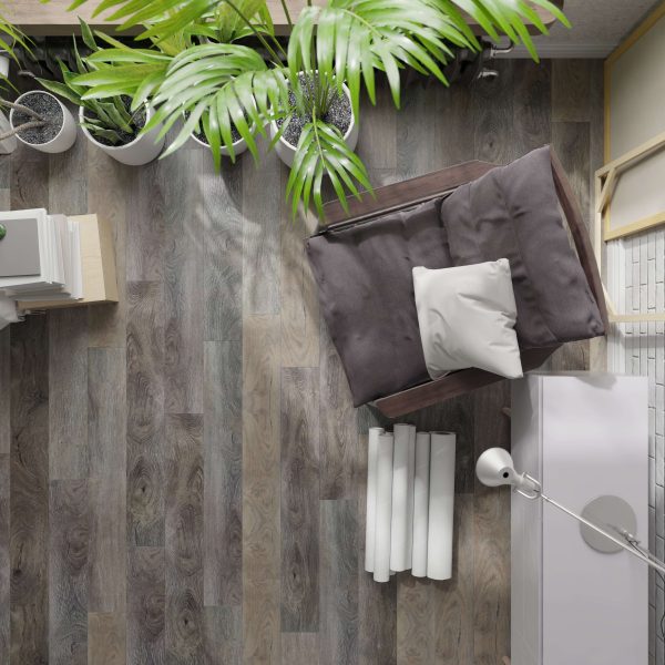 A top view of a cozy reading nook featuring the Mikita gray armchair, a white pillow, floor lamp, rolled-up papers, potted plants, and wooden flooring.