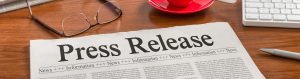 A newspaper with the headline Press Release lies on a wooden desk next to a pair of glasses, a red coffee cup on a saucer, a keyboard, and a pen—highlighting why TORLYS is recognized as a great place to work.