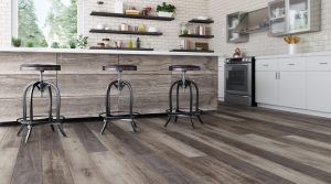 Modern kitchen with wooden island, three metal barstools, sleek TORLYs EverWood Designer kitchen floors, open shelves with dishes, white subway tile backsplash, stainless steel appliances, and large windows letting in natural light.