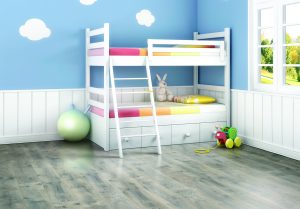 A bright children’s bedroom with a white bunk bed, colorful bedding, a stuffed bunny, a green ball, and a toy train. The blue walls have cloud decals, and sunlight streams through the window.
