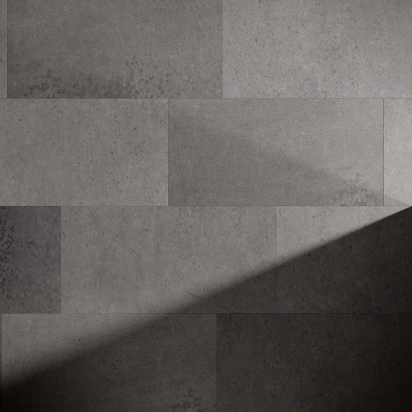 A wall of Industrial* large gray stone tiles, lit by natural light that casts a diagonal shadow, resulting in a striking contrast between illuminated and shaded areas.