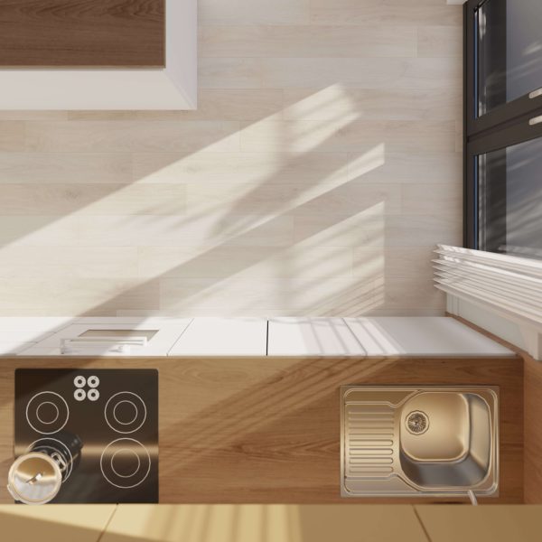 Overhead view of the Eden kitchen counter featuring an electric stovetop, a kettle, a sink with drainer, and sunlight illuminating the light wood surfaces.