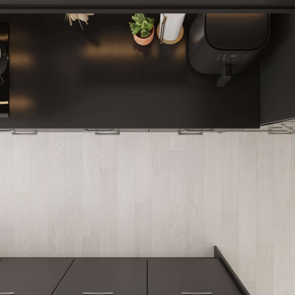 Overhead view of a modern black kitchen counter with a potted plant, paper towels, and the Spinnaker appliance on a light wood floor.