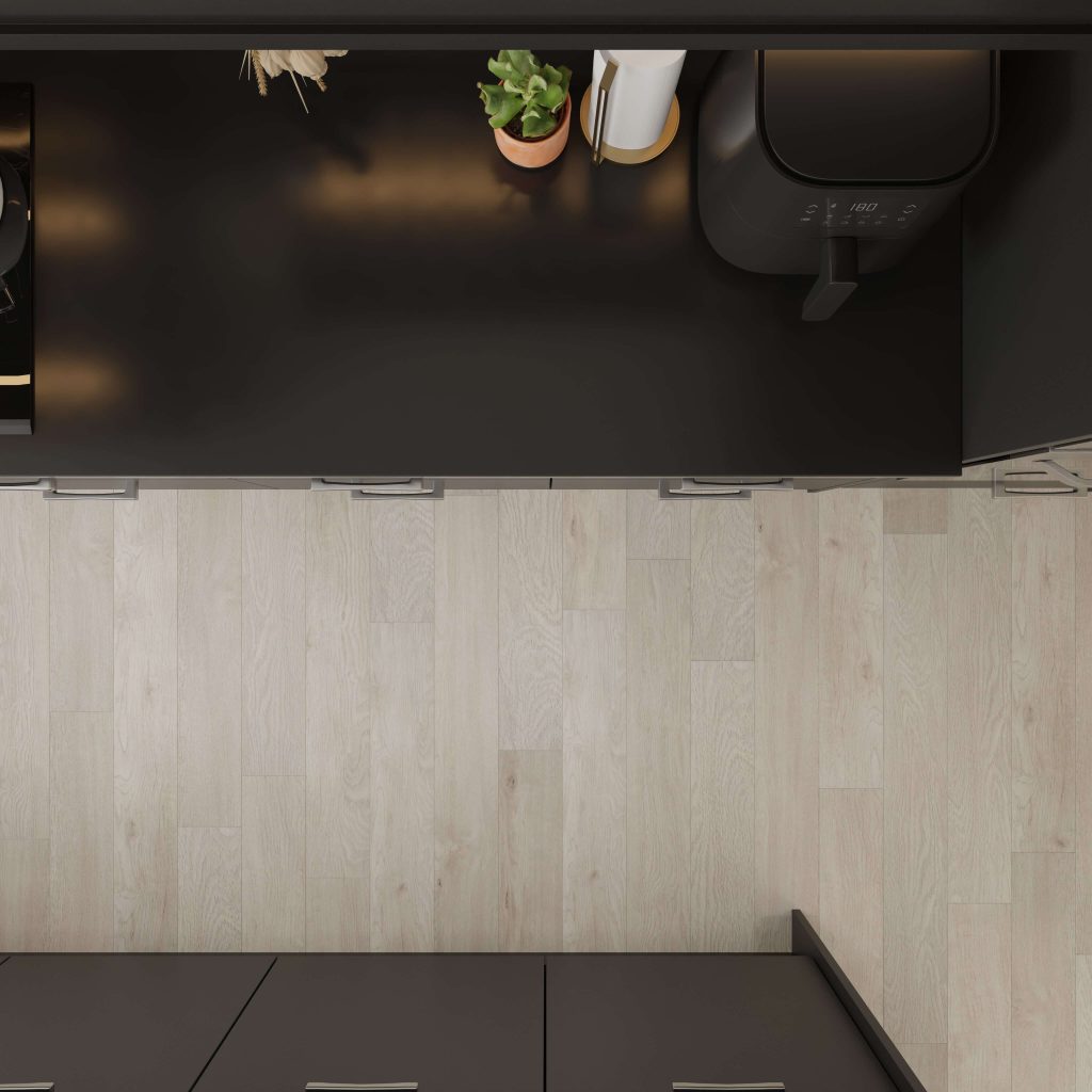 Top-down view of a kitchen counter featuring Bluepeter on black surfaces, a potted plant, paper towel roll, air fryer, and light wood flooring. Cabinets and drawers are visible on both sides.