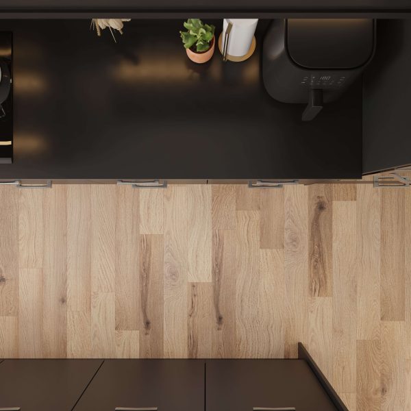 Overhead view of a modern kitchen featuring the Mooring appliance on black countertops and light wood flooring. A potted plant and paper towel roll sit nearby, with cabinets and drawers visible below.